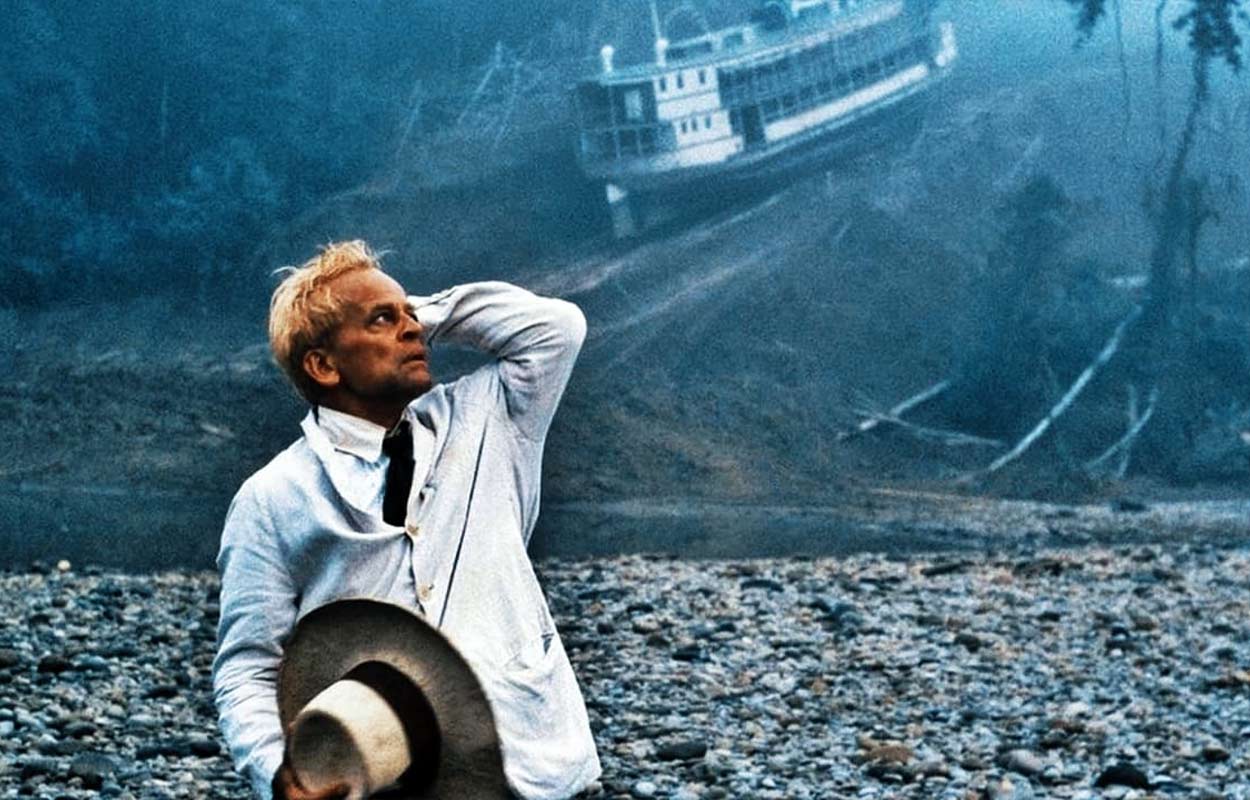 Klaus Kinski bär vit kostym och i bakgrunden ser vi fartyget släpas över berget.