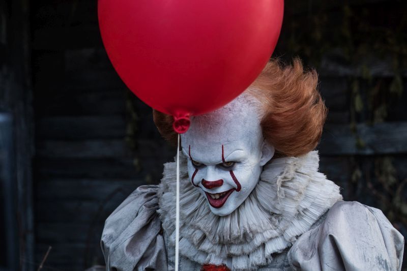 Bill Skarsgård som clownen Pennywise i skräckthrillern Det. En röd ballong svävar framför honom. 