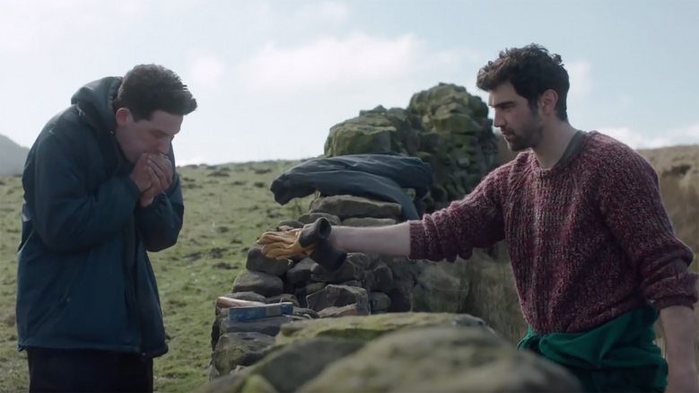 Från "God's Own Country" av Francis Lee. Två män står på varsin sida av en stenmur.