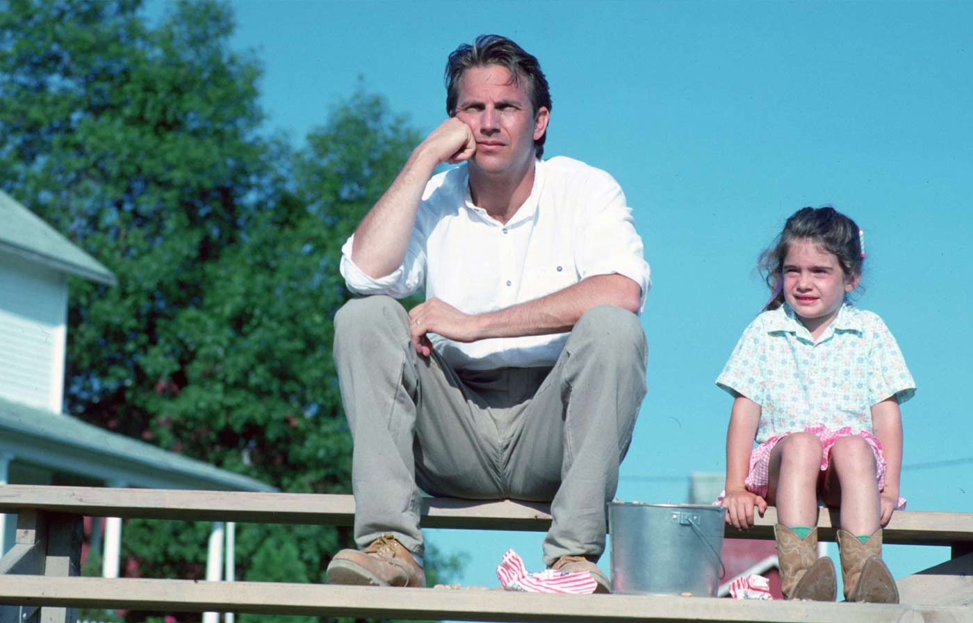 Kevin Costner sitter på en bänk och funderar